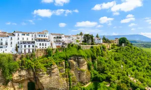 Vita hus i Ronda, Spanien, klättrar uppför en grönskande klippa under en blå himmel med moln.