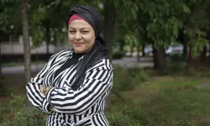 Zeina Mourtada, med en svart och röd turban och en randig jacka, står med armarna i kors utomhus.
