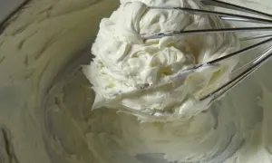 Un fouet de cuisine retient une généreuse portion de glacage mascarpone crémeux, prêt à garnir un gâteau.