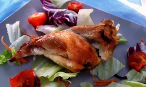 Un succulento coniglio allo spiedo, dorato e croccante, adagiato su un letto di insalata fresca con pomodorini e carote.