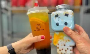 Zwei Hände halten leckere Getränke: ein Bubble Tea von Mr. Box Tea in Berlin und ein süßer blauer Drink in einer Figurenflasche.