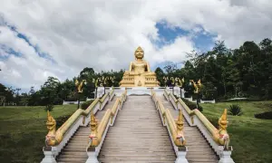 Goldene Buddha-Statue über einer langen Treppe mit Naga-Schlangen-Geländern in Nakhon Si Thammarat.