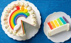 Torta arcobaleno con decorazioni colorate e una fetta servita su un piatto.
