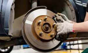 Gros plan sur un disque de frein rouillé et une plaquette de frein usée, tenue par une main gantée, prête pour le remplacement.