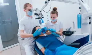Dentysta z mikroskopem i asystentka pracują przy pacjentce. Zabieg stomatologiczny, być może z użyciem devipasta, przebiega precyzyjnie.