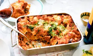 En nybakad vegetarisk lasagne i formen, toppad med ost och persilja. Ett glas rödvin står bredvid.