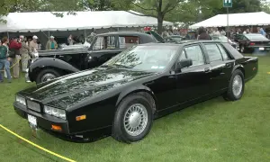 Svart Aston Martin Lagonda står på gräsmatta vid ett evenemang med tält och folk i bakgrunden.