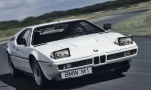 Białe BMW M1 z lat 80. pędzi po krętej drodze, ukazując swój kultowy design.