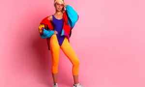 Dziewczyna w neonowym stroju i kolorowej kurtce, z opaską na włosach i okularach, prezentuje styl lat 90.