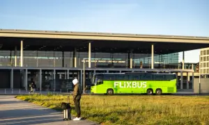 Mann mit Koffer wartet auf den Flixbus am Flughafen Berlin Brandenburg. Eine Direktverbindung Dresden Berlin Flughafen ist hier möglich.
