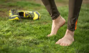 Stopy na trawie, obok leżą buty. Czas na bieganie boso, poczuj ziemię pod stopami.