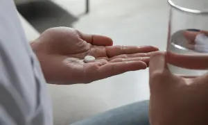 En hand håller en tablett, redo att sväljas med ett glas vatten. Detta kan vara en del av förklaringen till hur funkar antidepressiva.