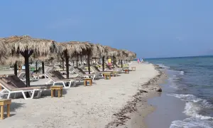 Piękna plaża Tigaki z rzędami leżaków pod słomianymi parasolami, spokojne morze i błękitne niebo.
