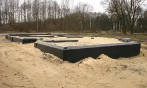 Odkopanie i izolacja fundamentów domu w piaskowym terenie. Czarna folia zabezpiecza ściany.