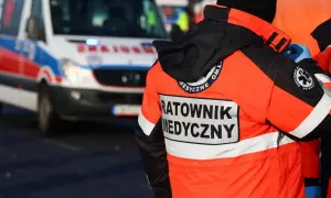 Ratownik medyczny w pomarańczowej kurtce z napisem "RATOWNIK MEDYCZNY" stoi obok karetki. Zastanawiasz się, ile zarabia ratownik medyczny?