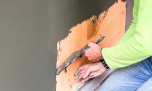 Pracownik nakłada zaprawę na siatkę zbrojeniową. Poznaj atrakcyjną tynkowanie cena.