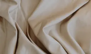 Sanfter, beige Stoff fällt in weichen Falten. Lyocell ist das, ein nachhaltiges Material, das sich so angenehm anfühlt.