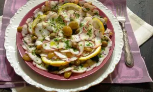 Delizioso carpaccio di polpo con limone, olive e capperi, condito con erbe fresche e olio d'oliva. Un piatto leggero e saporito.