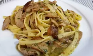 Un piatto invitante di tagliatelle ai porcini, condite con funghi freschi e prezzemolo tritato, su un piatto bianco.