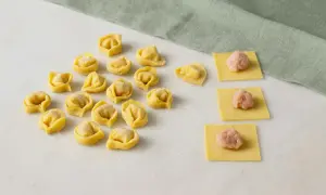 Frische Tortellini und Teigquadrate mit Füllung auf Marmorplatte.