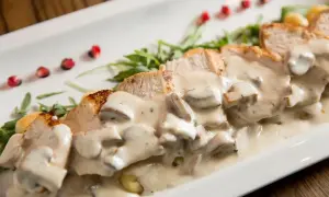 Pokrojony kurczak w sosie pieczarkowym z rukolą i pestkami granatu na białym talerzu.