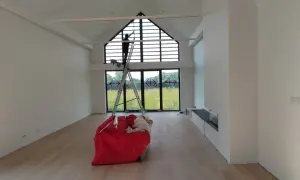 Prace remontowe w przestronnym wnętrzu. Na drabinie stoi osoba, która prawdopodobnie sprząta, zastanawiając się, czym usunąć pył gipsowy.