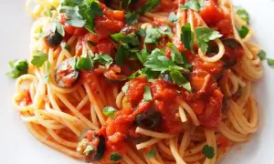 Pyszny makaron spaghetti z sosem pomidorowym, oliwkami i natką pietruszki. Czy makaron do spaghetti się płucze? Zazwyczaj nie, aby sos lepiej przylegał.