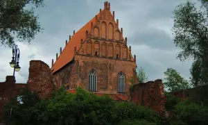 Gotycka ceglana bazylika z czerwonym dachem, ruiny murów obronnych i zieleń. To jedno z miejsc, co zobaczyć w Elblągu.