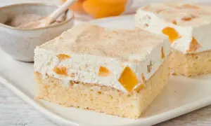 Saftiger Pfirsich Schmand Kuchen mit Zimt bestreut, serviert auf einem weißen Teller.