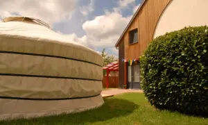 Une yourte alsace, à côté d'une maison en bois, sous un ciel bleu et nuageux.