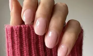 Delikatne, różowe paznokcie w stylu "soap nails" lśnią na tle grubego, różowego swetra.