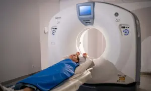 Pacjentka leży na stole tomografu, przykryta niebieskim fartuchem. Nie trzeba się rozbierać do tomografii, wystarczy zdjąć metalowe przedmioty.