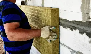 Pracownik montuje wełnę mineralną na ścianie. Ocieplenie wełną cena robocizny jest kluczowa dla budżetu.