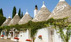 I trulli di Puglia, con i loro tetti conici e le decorazioni bianche, incantano sotto il cielo azzurro, avvolti dal verde rampicante.