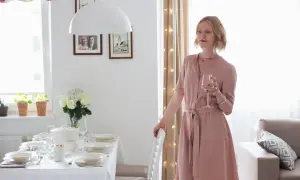 Elegancka kobieta w różowej sukience z kieliszkiem wina, przy nakrytym stole. Idealna stylizacja co na wesele.