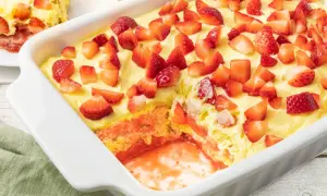 Tiramisù fragole in una teglia bianca, con strati di crema, biscotti e tante fragole fresche a pezzi.