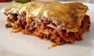 Kawałek zapieczonej lasagne z ciągnącym się serem na białym talerzu.