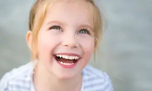 Uśmiechnięta dziewczynka z blond włosami, której radość przypomina o sile ducha w walce z zespołem Angelmana.