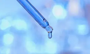 Kropla błękitnego serum, zawierającego peptyd miedziowy, spływa z pipety na rozmyte, błękitne tło.