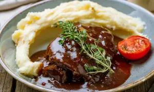 Pyszny schab w sosie własnym, podany z kremowym purée ziemniaczanym i pieczonym pomidorkiem.