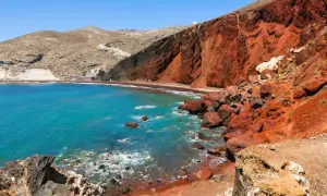 Santorini plaże: turkusowe morze obmywa czerwoną, wulkaniczną plażę, otoczoną skalistymi klifami.