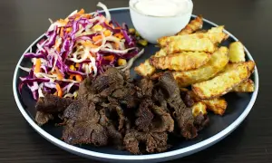 Talerz z mięsem kebab, frytkami, surówką z czerwonej kapusty i sosem.