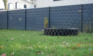 Moderne Zaun-Sichtschutz-Ideen: Dunkelgrauer Lamellenzaun mit dekorativem Feuerring im Garten.