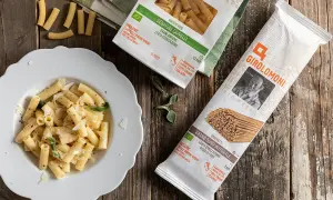 Piatto di maccheroni conditi e pacchi di pasta della Gino Girolomoni Cooperativa Agricola, con grano italiano.