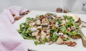 Wykwintna sałatka z gruszką i gorgonzolą, orzechami włoskimi i rukolą, podana na białym talerzu.