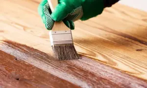 Mano con guante verde aplicando barniz a madera. Proceso para saber como impermeabilizar madera y protegerla.