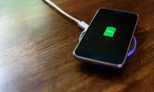 Smartfon na drewnianym blacie, wskaźnik pokazuje 100% – zakończone ładowanie baterii.