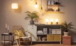Mysig belysning vardagsrum med en flätad stol, en byrå fylld med böcker och förvaring, samt växter.