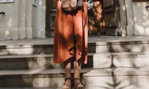 Kobieta w pomarańczowej sukience i sandałach trzyma książkę. Stylizacja idealna do letniego lookbooka.