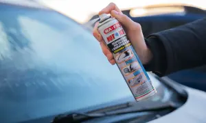 Mano che spruzza un prodotto per togliere il ghiaccio dal parabrezza dell'auto.